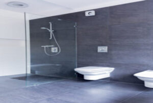 Luxurious grey bathroom with large granite tiles on the floor and walls, and glass shower screen